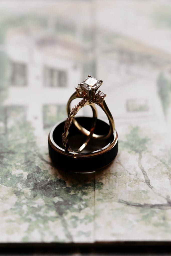 Close-up of engagement and wedding rings stacked together on painted stationery with soft natural light.