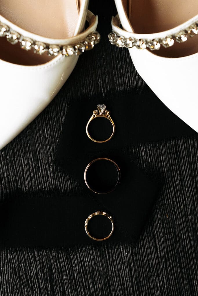 Wedding bands reflected beneath embellished bridal shoes in a minimalist wedding detail photo.