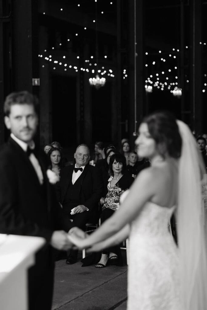 Bride and groom stand at the altar while family members watch from the front row during an industrial wedding ceremony.