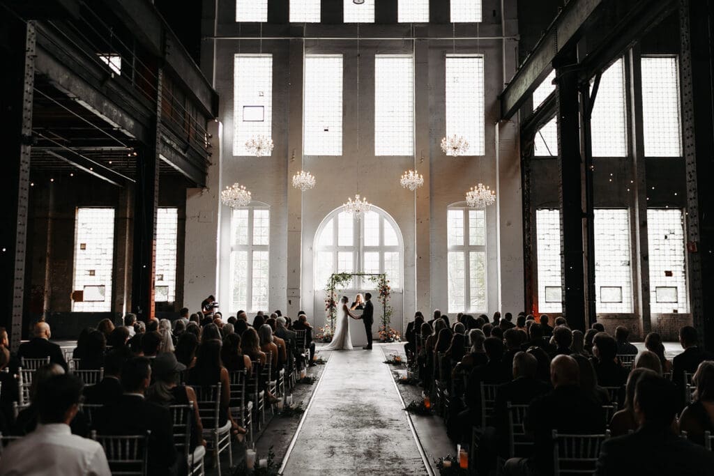 Wide view of an industrial wedding ceremony featuring a dramatic long aisle, one of the most overlooked wedding photo tips for creating dynamic ceremony imagery.