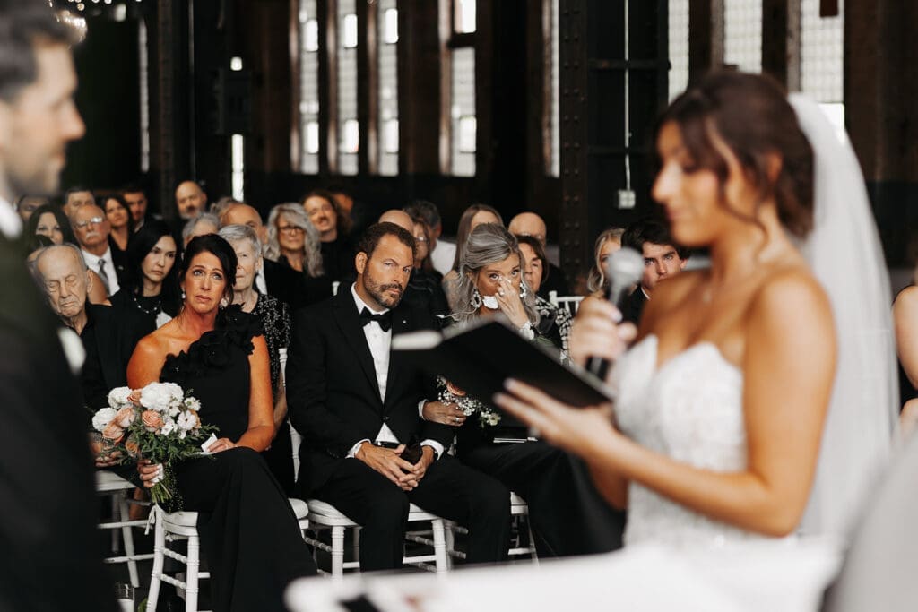 Bride reads her vows during the ceremony as emotional family members listen from the front row, a meaningful moment often preserved through wedding photography and videography packages.