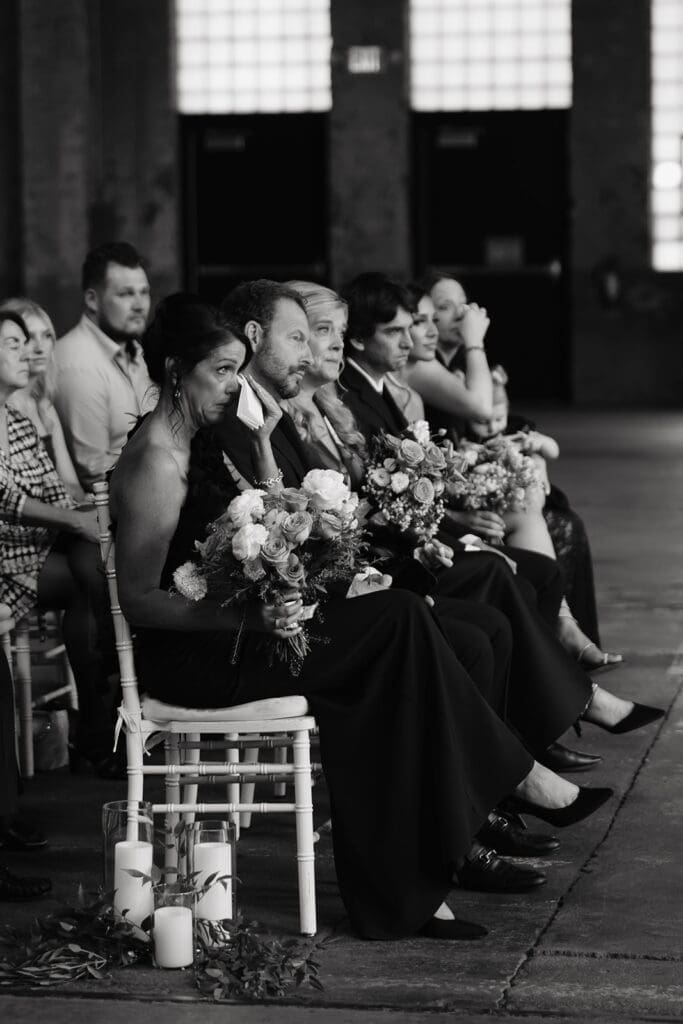 Wedding party members sit together during the ceremony while watching the couple exchange vows inside a historic venue.