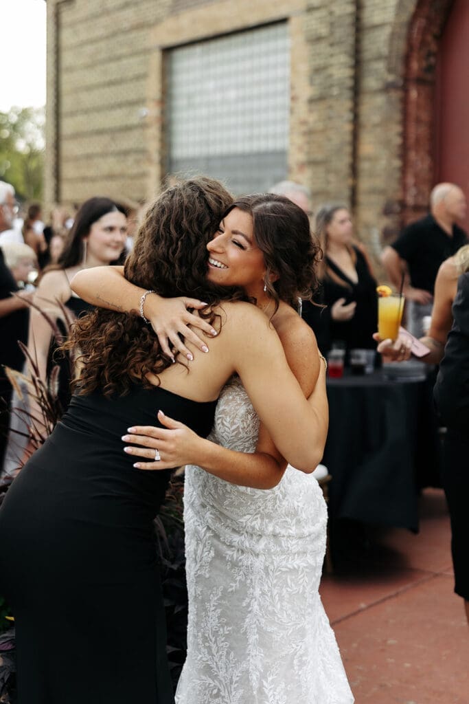 Bride hugs a guest during cocktail hour after enjoying a relaxed wedding day timeline with a first look.