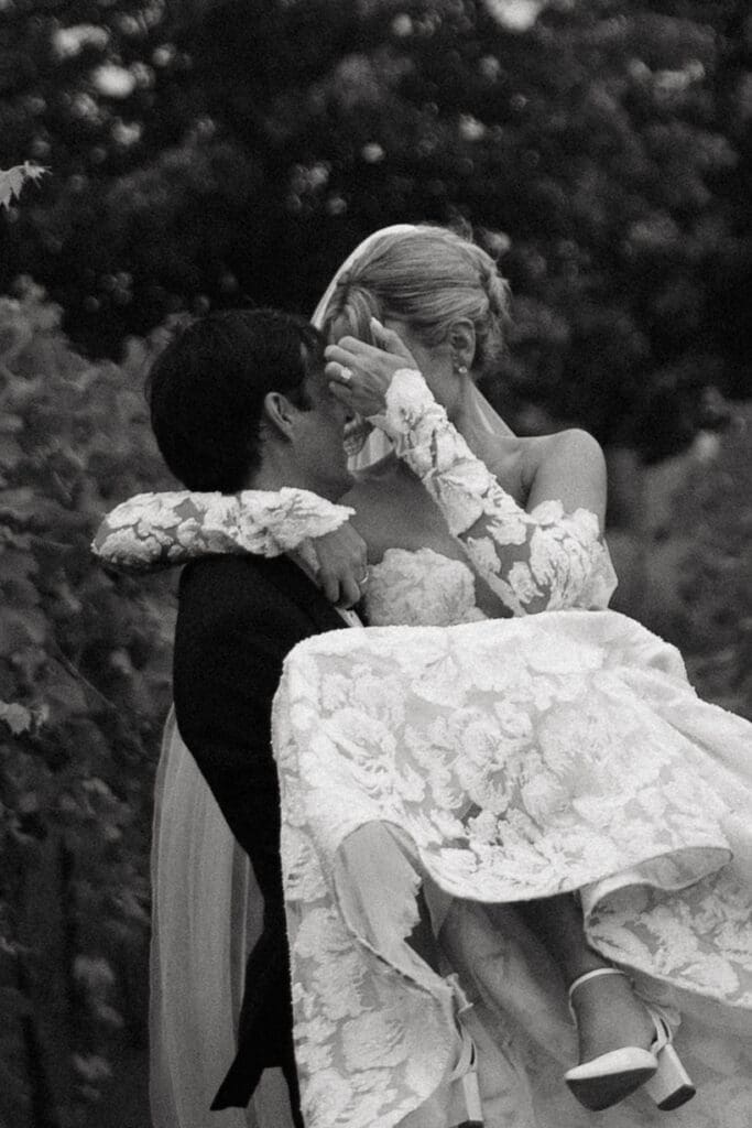 Groom carrying his bride through the vineyard while she laughs and brushes hair from her face during sunset portraits.