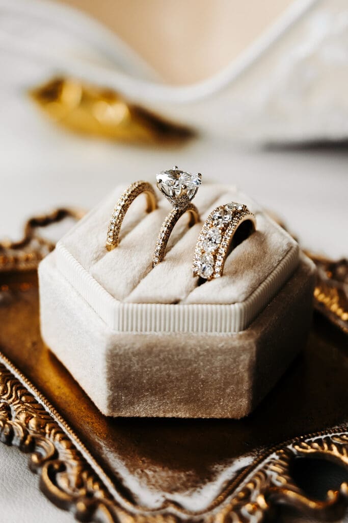 Diamond engagement ring and wedding bands styled in a velvet ring box atop an ornate brass tray.