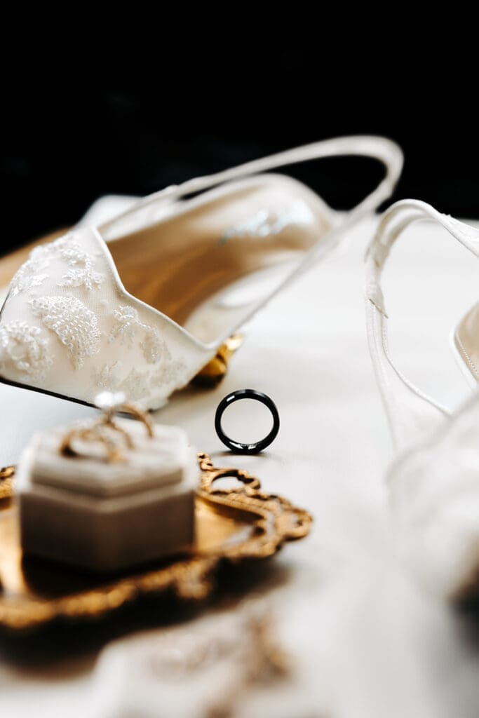Embroidered bridal shoes, ring box, and wedding band styled in soft natural light.