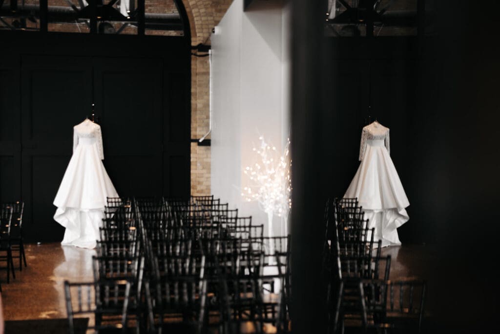 Wedding gown hanging alone in a dramatic industrial ceremony space before guests arrive.