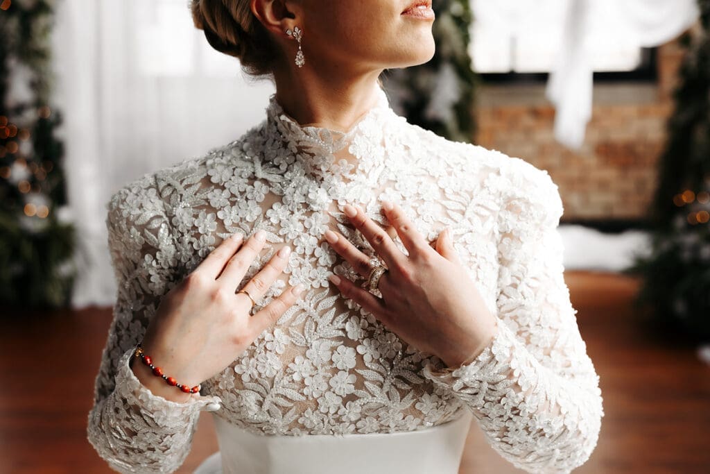 Close-up portrait highlighting the intricate lace texture, heirloom jewelry, and craftsmanship of a bridal gown.