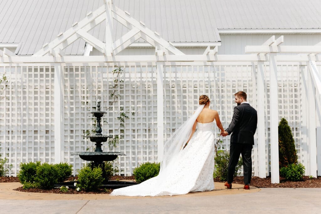 Bride and groom walking beneath the white pergola outside this elegant blank canvas wedding venue in Minnesota.