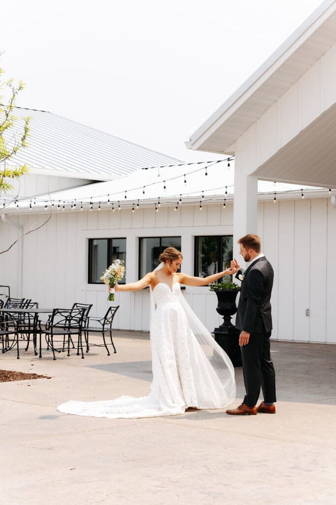 Bride steps back for groom to look at her fully during their first look photos at Equestria West at Bavaria Downs in Minnesota.