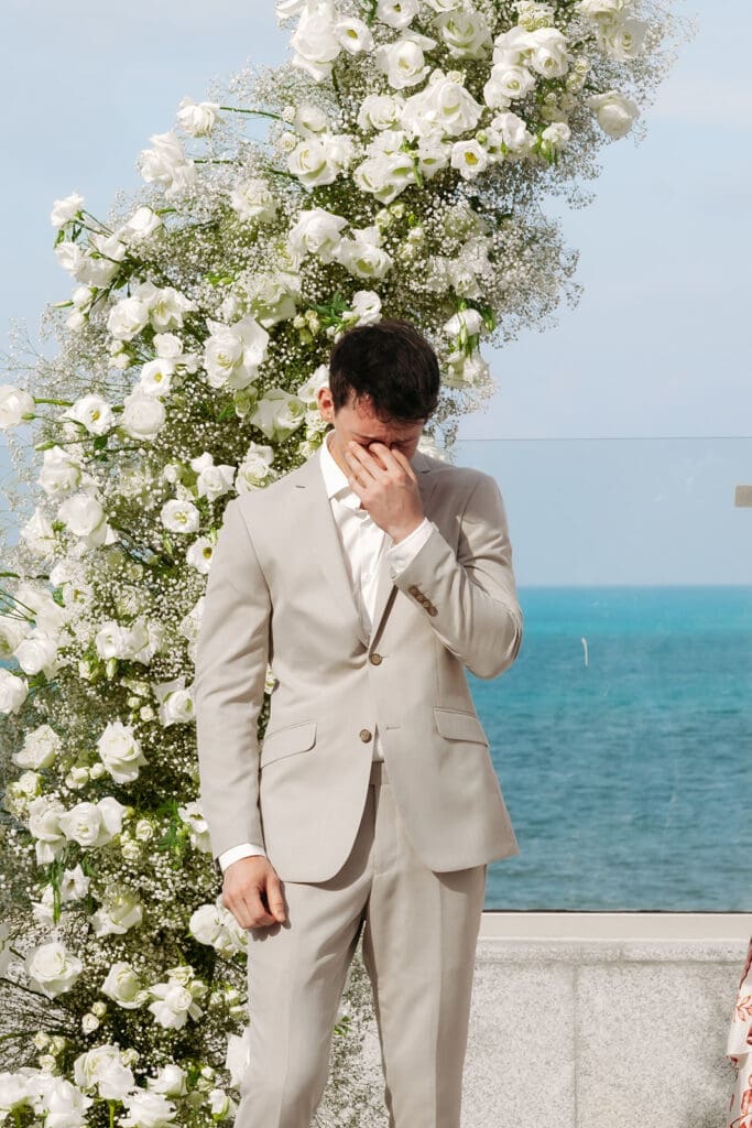 Groom wipes away tears while waiting for his bride during an emotional wedding ceremony by the ocean at Grand Palladium Select Costa Mujeres 