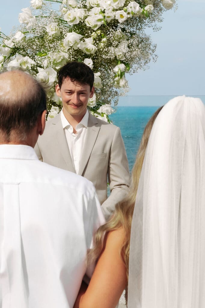 Groom smiles as his bride walks toward the ceremony following a meaningful wedding first look before exchanging vows.