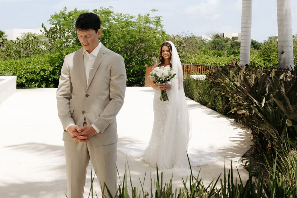 Bride walks toward her groom moments before their intimate destination wedding first look in a sunlit courtyard at Grand Palladium Select Costa Mujeres in Mexico.